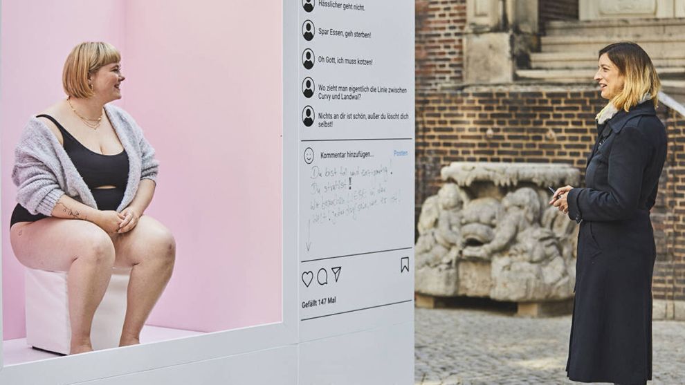 Eine Frau sitzt in einem offenen Kasten, der wie ein Social Media Post gestaltet ist, und spricht mit einer anderen Frau.