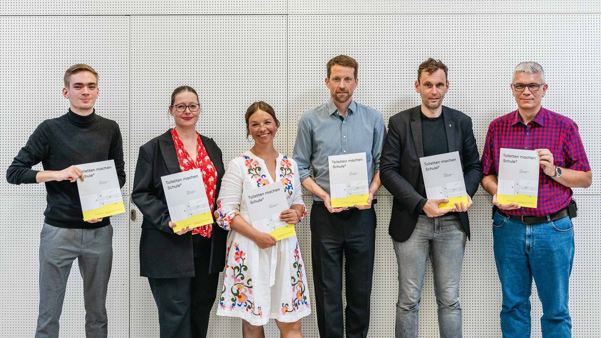 Sechs Personen halten Exemplare der Studie zu den deutschen Schultoiletten in der Hand, die von Domestos unterstützt wurde.