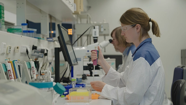 Eine Frau in einem Laborkittel und mit Schutzbrille benutzt eine Pipette.