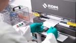 Ein Wissenschaftler aus der Forschung und Entwicklung von Unilever führt in weißem Laborkittel und grünen Handschuhen eine Papierverpackungsprobe in eine Maschine ein.