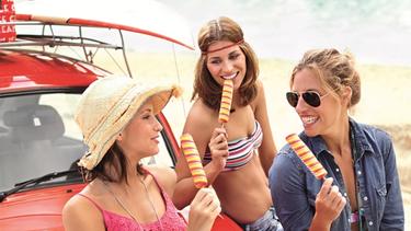 Drei lächelnde Frauen in Sommerkleidung essen Eis und versprühen Lebensfreude und Spaß.