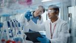 Eine Wissenschaftlerin und ein Wissenschaftler betrachten blaue Flüssigkeit in Laborkolben.