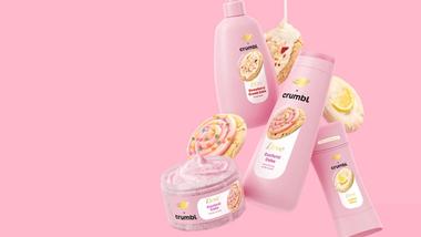 Ein Bild der Crumbl-Produkte von Dove, darunter Strawberry Crumb Cake, Confetti Cake und Lemon Glaze, vor einem rosafarbenen Hintergrund.