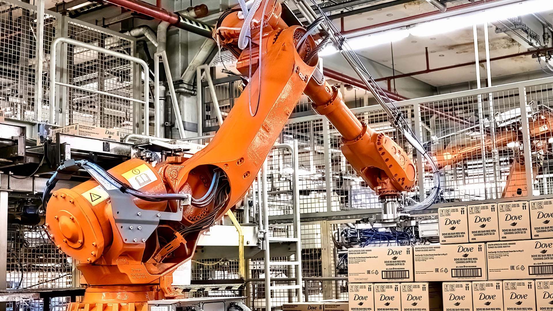 Ein orangener Packroboter stapelt Kartons mit Dove-Waschstücken.