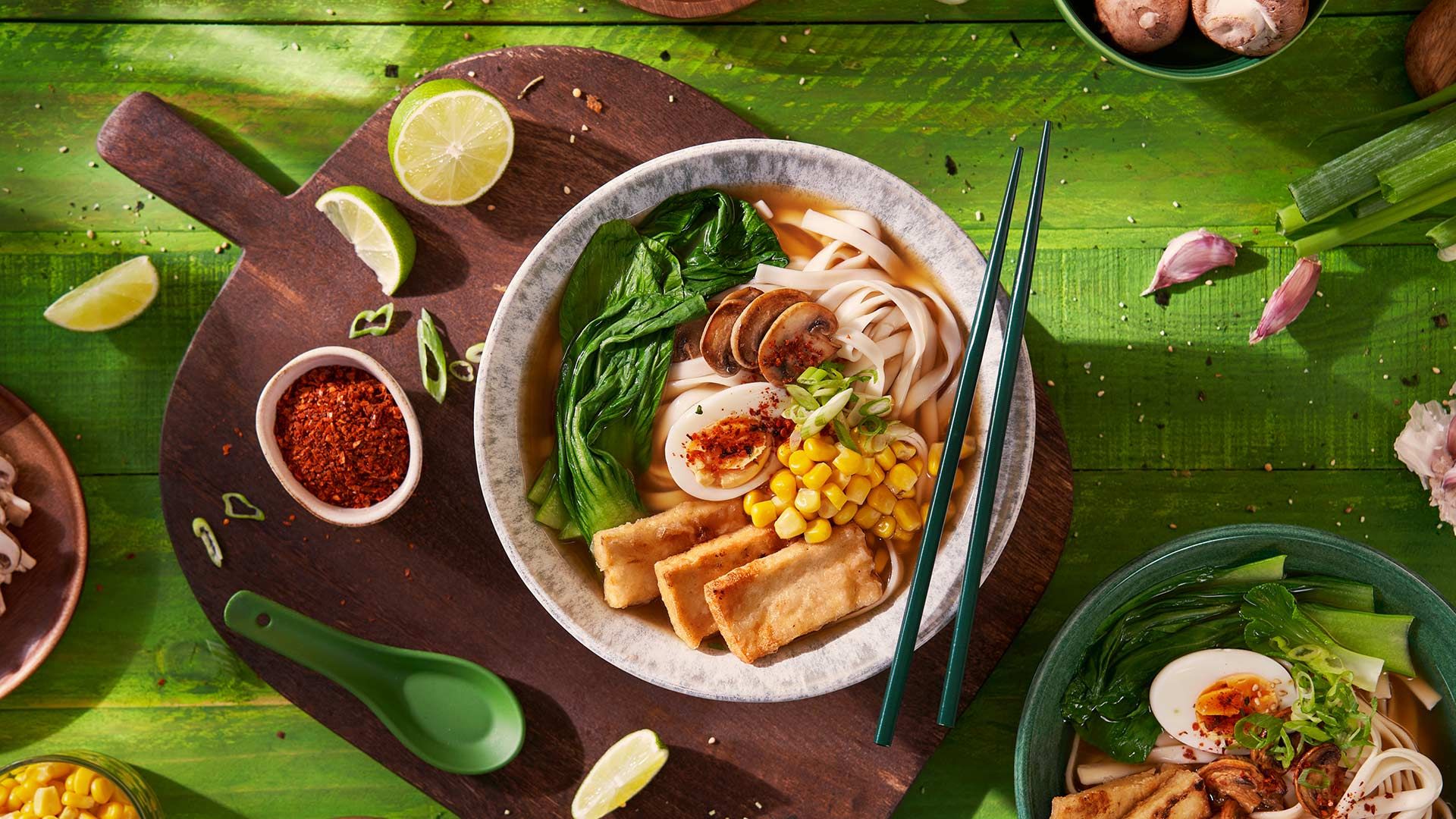 Auf einem Holzbrett ist ein mit Gemüse angerichteter Teller mit asiatischen Stäbchen zu sehen.