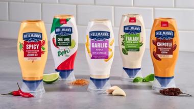 Verschiedene Hellmann‘s-Mayonnaisen in Dosierflaschen, dargestellt mit Hauptzutaten wie Limette, Chili, Knoblauch und Kräutern
